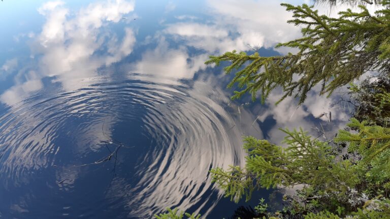 Wateroppervlak, met uitdeinende cirkels, dat de wolken uit de lucht spiegelt, symbool van bespiegelingen 